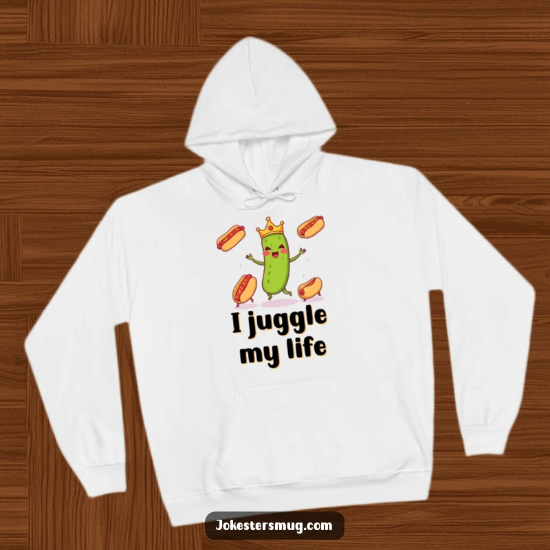 Funny pickle wearing a tiny crown enthusiastically juggling three runaway hot dogs, captured on a cozy hoodie for humorous warmth.